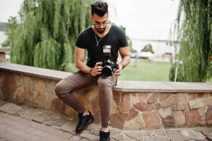 Awesome beautiful tall ararbian beard macho man photographer in glasses and black t-shirt with professional camera at hands.