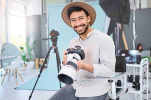 Portrait, photographer and man with camera in studio, happy and smile before a photo shoot. Face, photography and asian guy relax during professional, shooting for model, design and creative career.