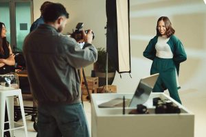 Photoshoot, studio and photographer with model on set for creative, about us or career. Media, production and female person with photography behind the scenes for fashion magazine cover with agency.